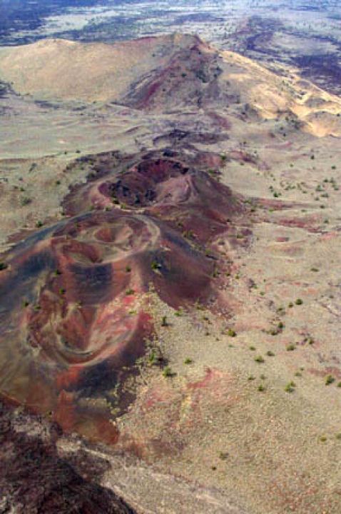 An aerial view looking down upon a desert landscape, punctuated by a series of large blackish craters.