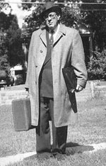 Black and white portrait of Howard Zahinser wearing a long coat and carrying a small suitcase and books. More about this picture plus a quote in the inset below.